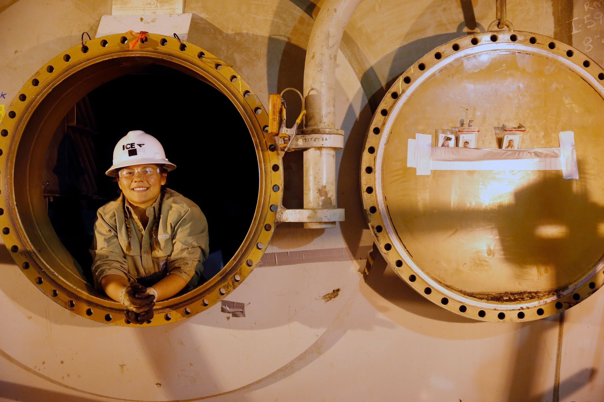 A man in a hard hat is looking out of a round window