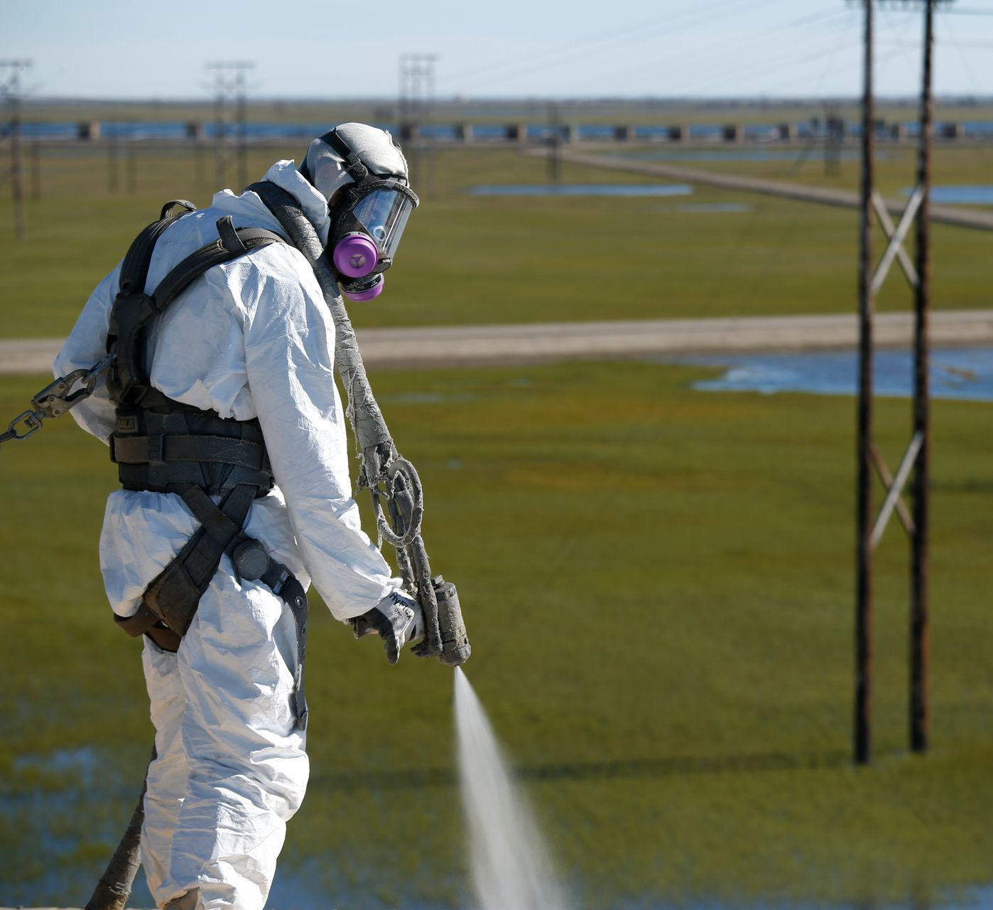 A man wearing a gas mask is spraying water in a field