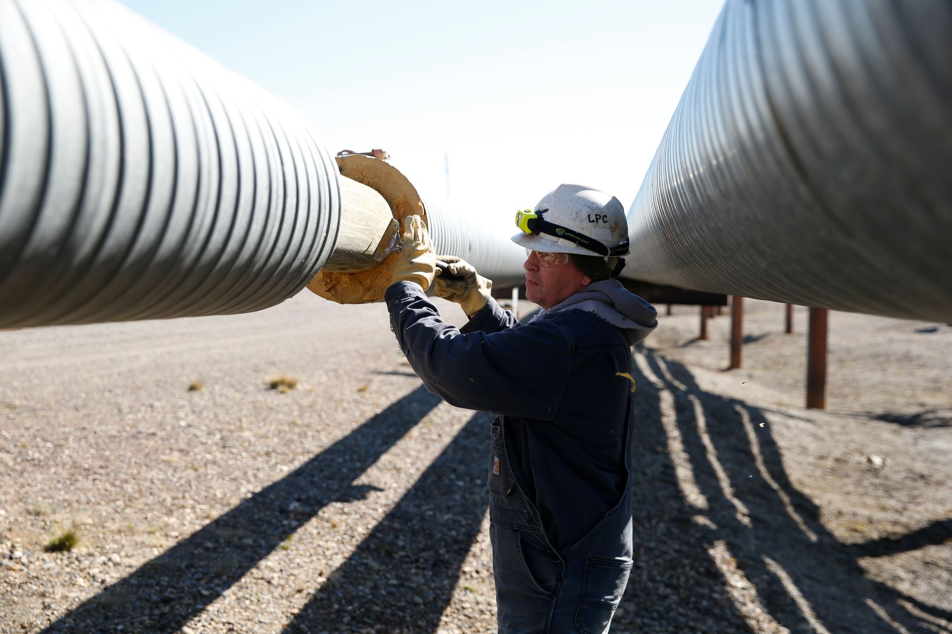 A man wearing a hard hat is working on a pipe