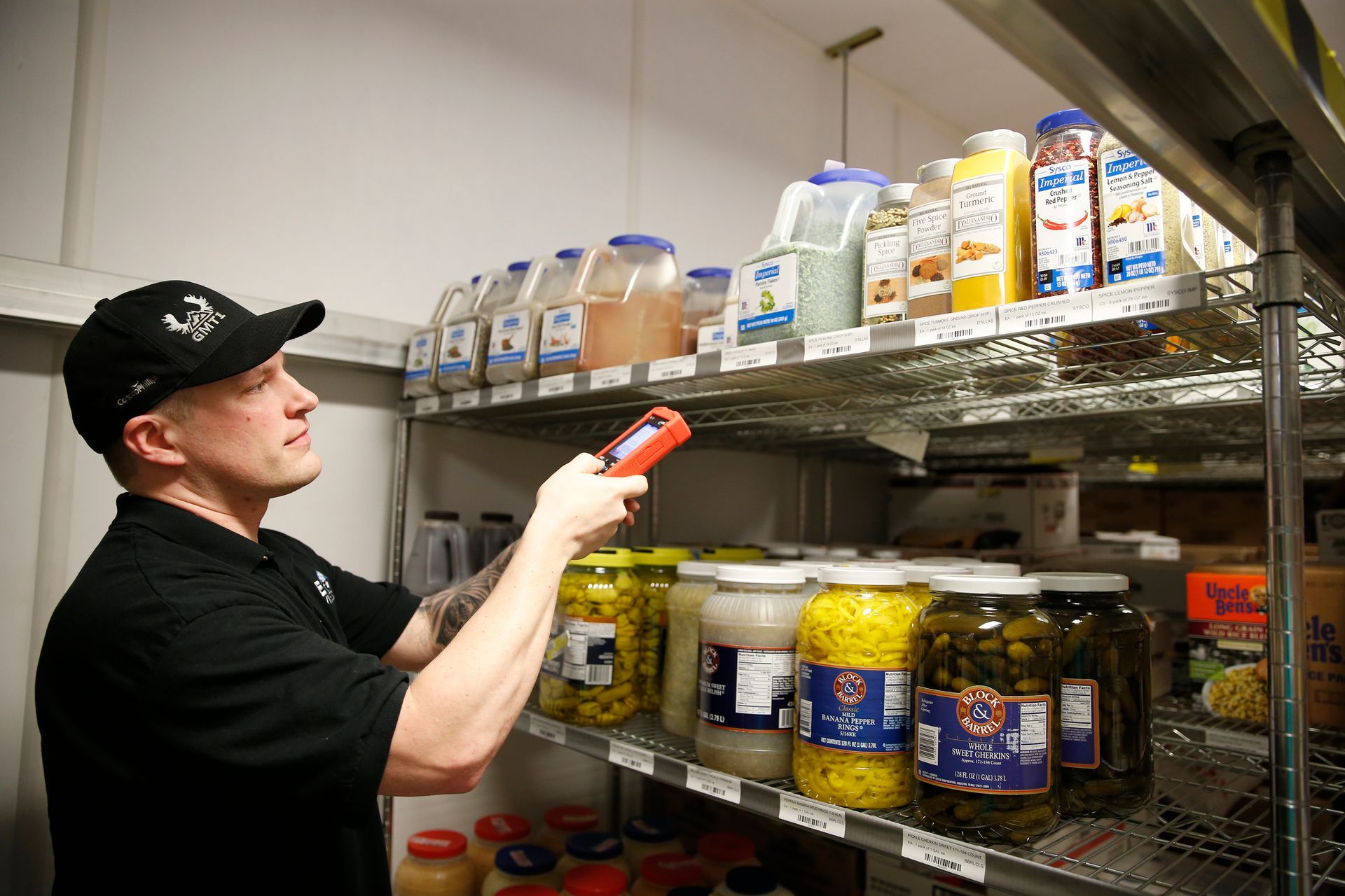 A man is taking a picture of a jar of pickles in a refrigerator.