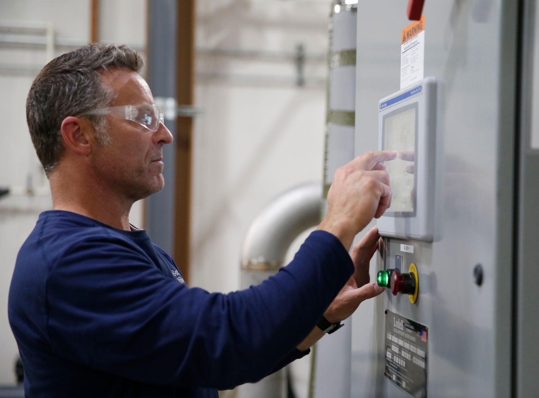 A man wearing safety glasses is working on a machine in a factory.