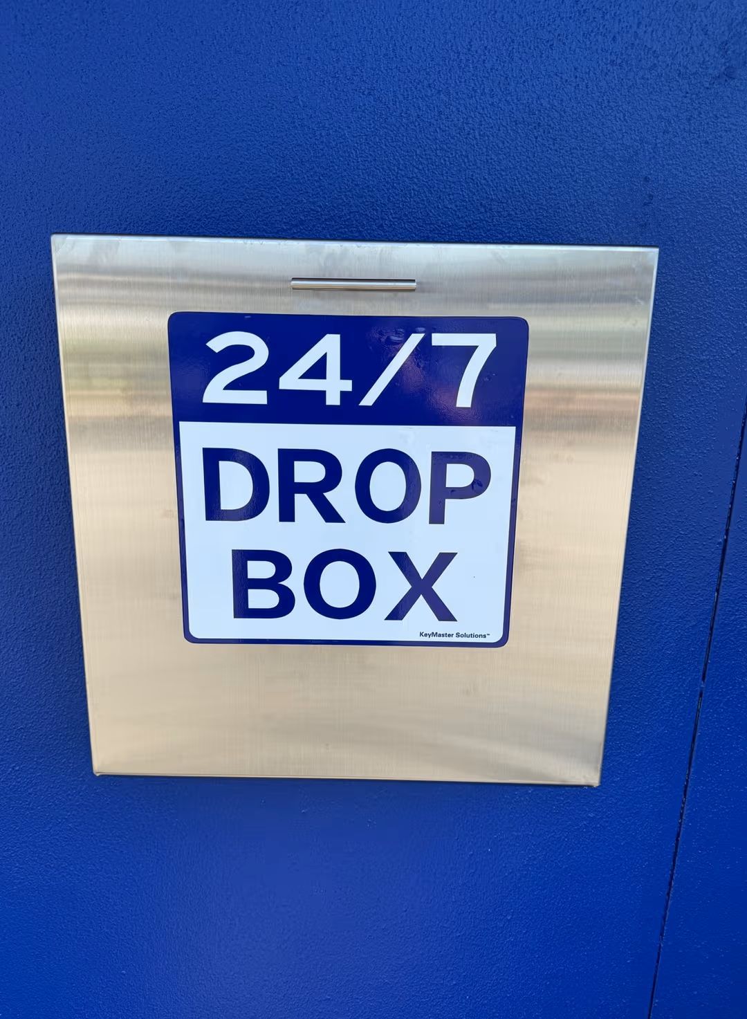24/7 drop box sign on a blue wall with a stainless steel box attached below it