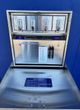 Wall-mounted stainless steel napkin dispenser and trash receptacle in a blue-walled restroom.