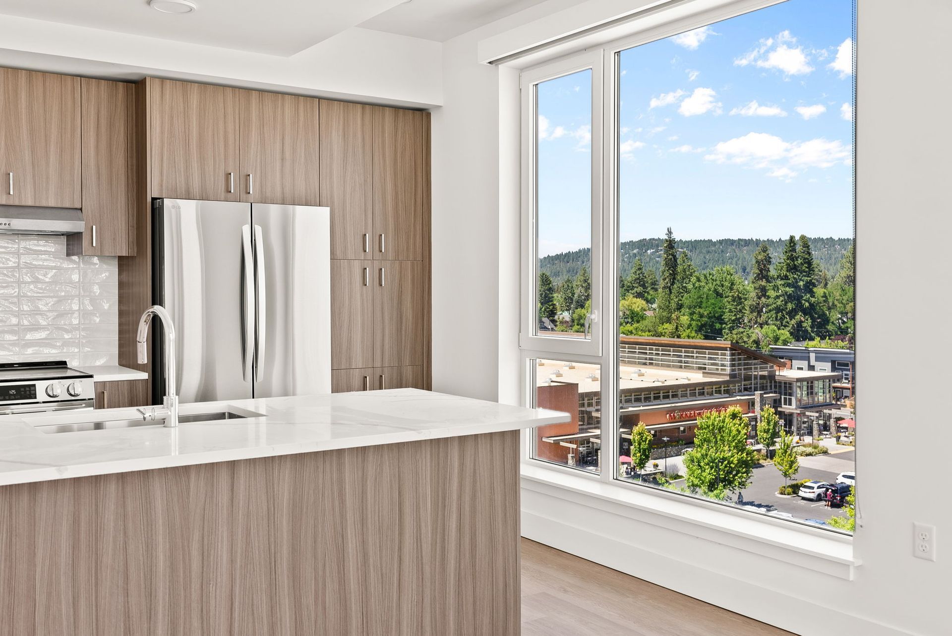 Modern kitchen with stainless steel appliances and large window overlooking a neighborhood.