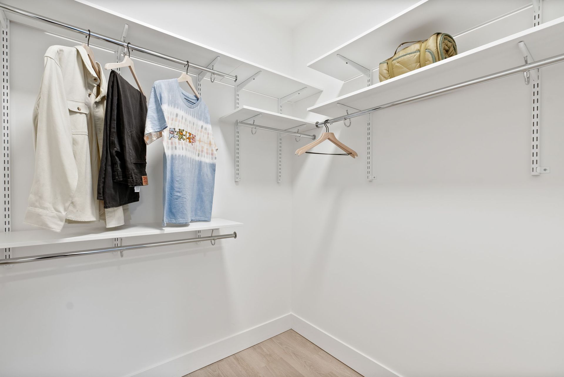White walk-in closet with hanging clothes, shelves with items, and a wooden floor.