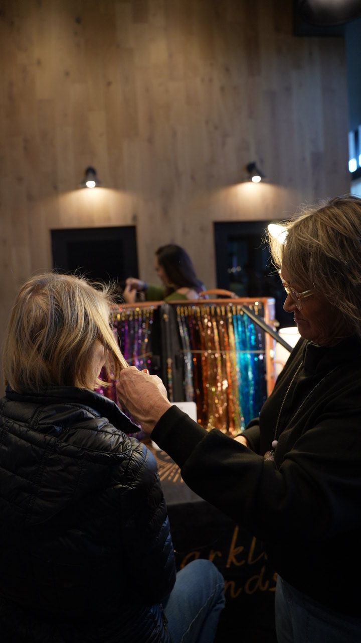 Person braiding another person's hair in a hair salon. Colorful hair extensions are in the background.
