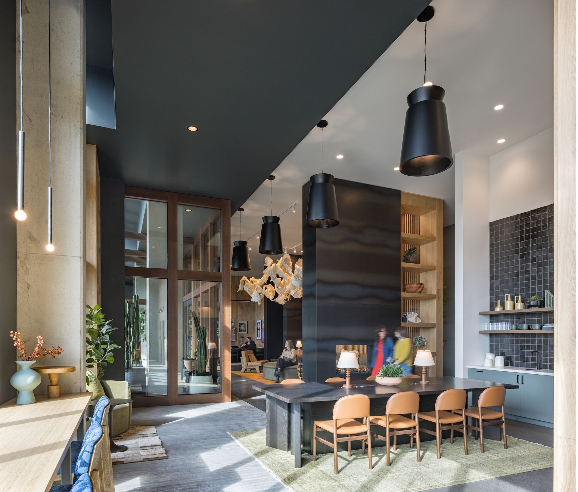 Modern lounge area with a long wooden table, leather chairs, and black pendant lights.