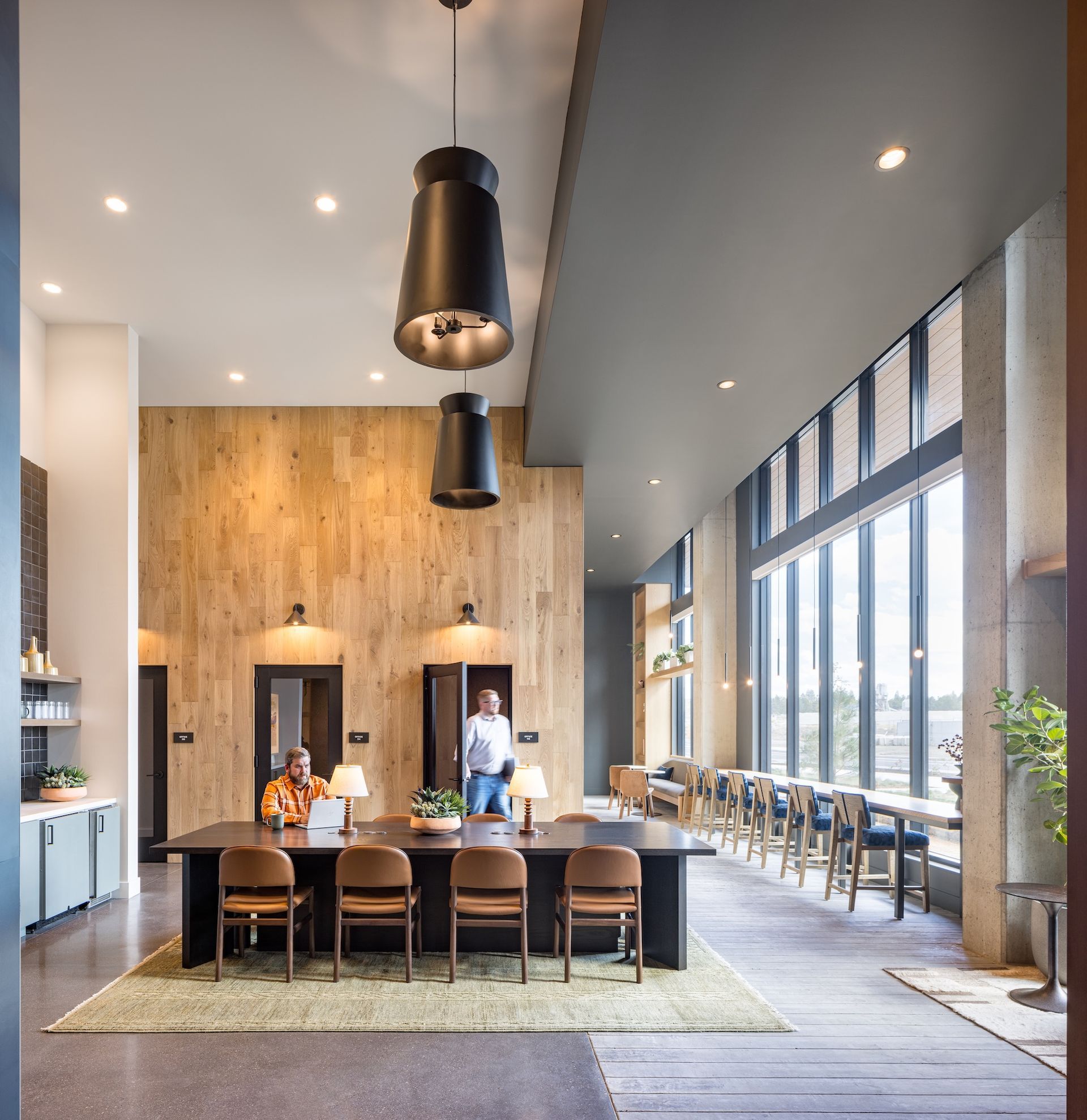 Modern office lobby with wood paneling, large windows, and people at a table.
