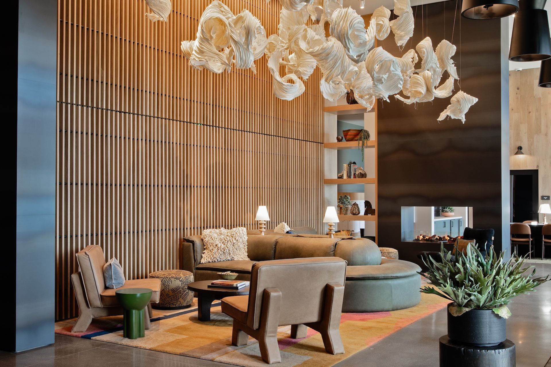 Lounge area with a couch, armchairs, and a colorful rug beneath a light fixture.