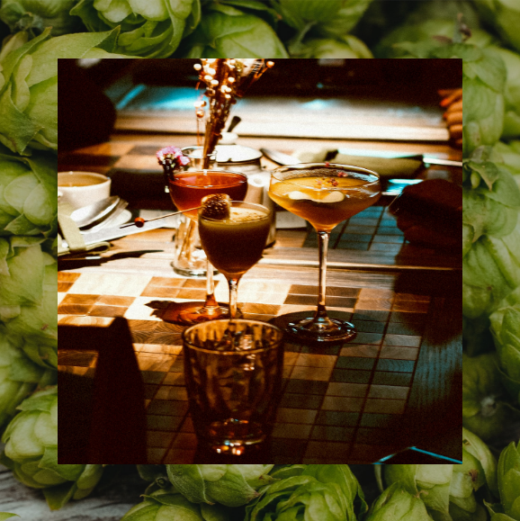 A table with glasses of wine and a martini surrounded by hops