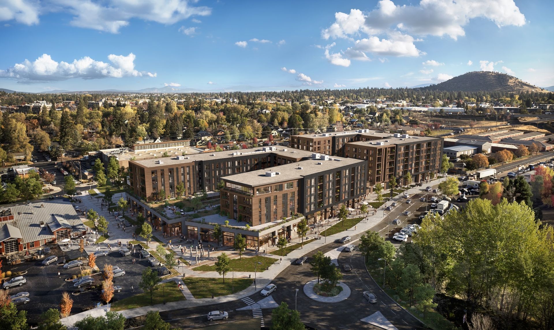 An aerial view of modern brown apartment buildings in an urban setting with a mountain in the background under a blue sky.