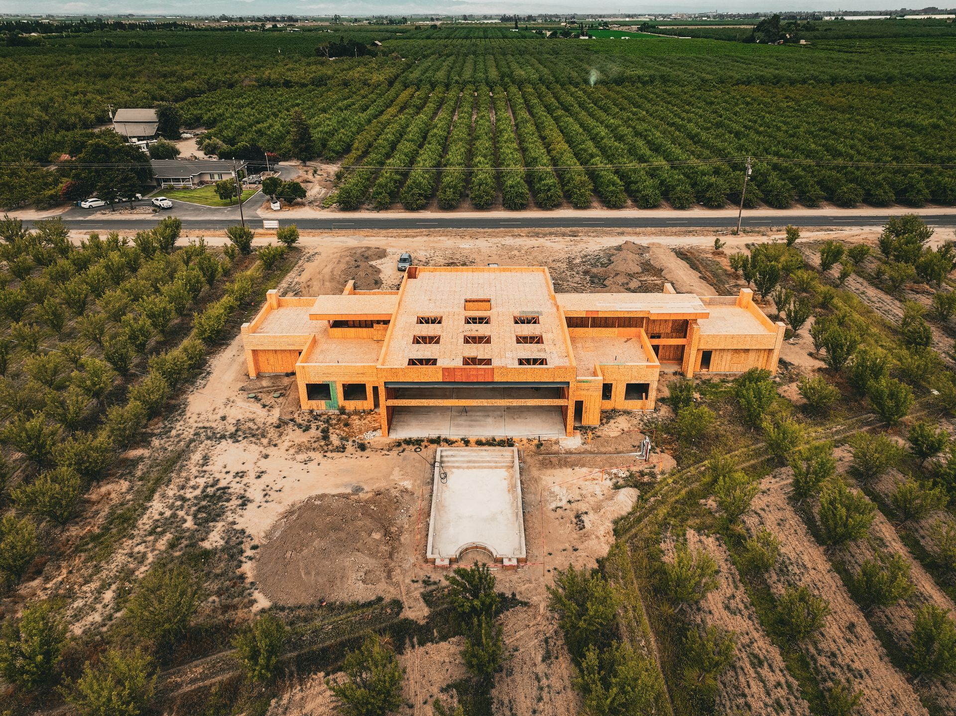 Aerial view of a large orange building amid orchards, with a road and dirt foreground.
