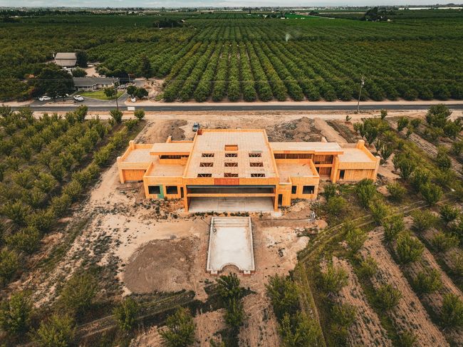 Aerial view of an orange building under construction amid orchard rows and dry land.