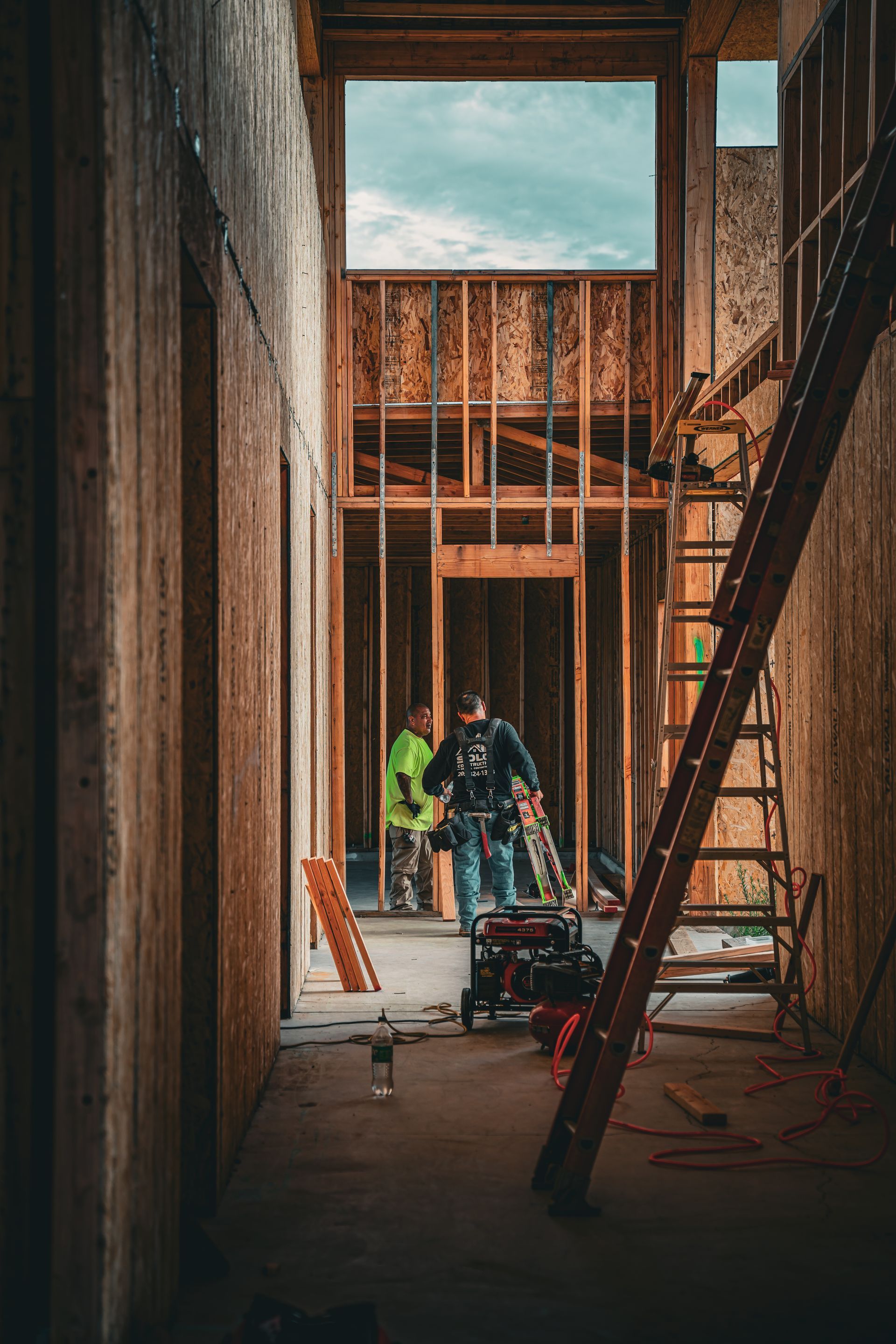 Construction workers in an unfinished building, with framing, ladders, and tools inside.
