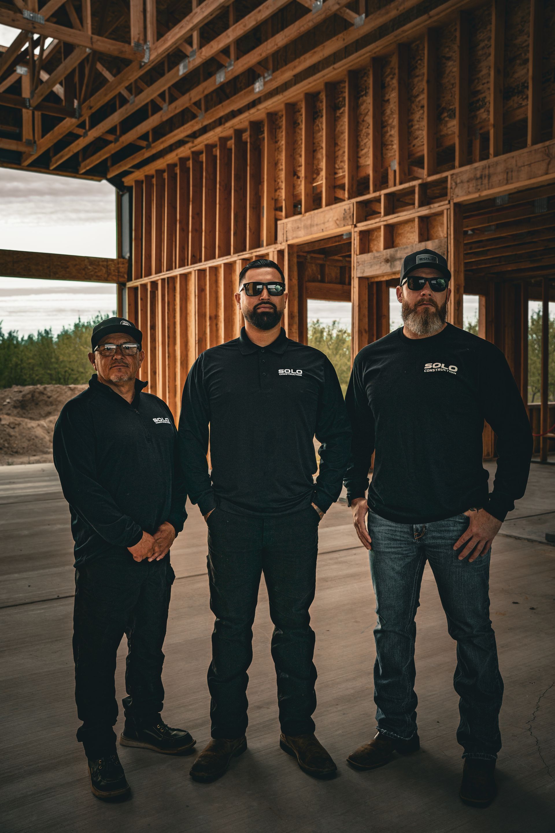Three people in black clothing standing inside an unfinished wooden building frame.