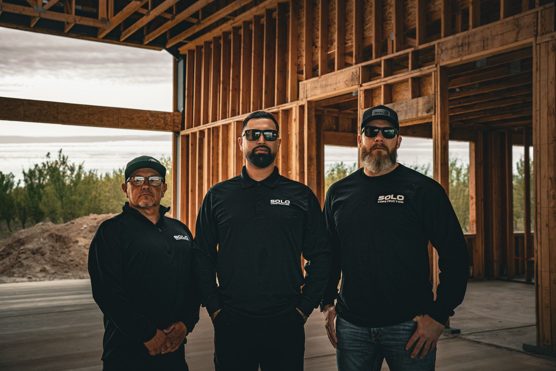 Three men in black shirts standing inside a wooden-framed building under construction.