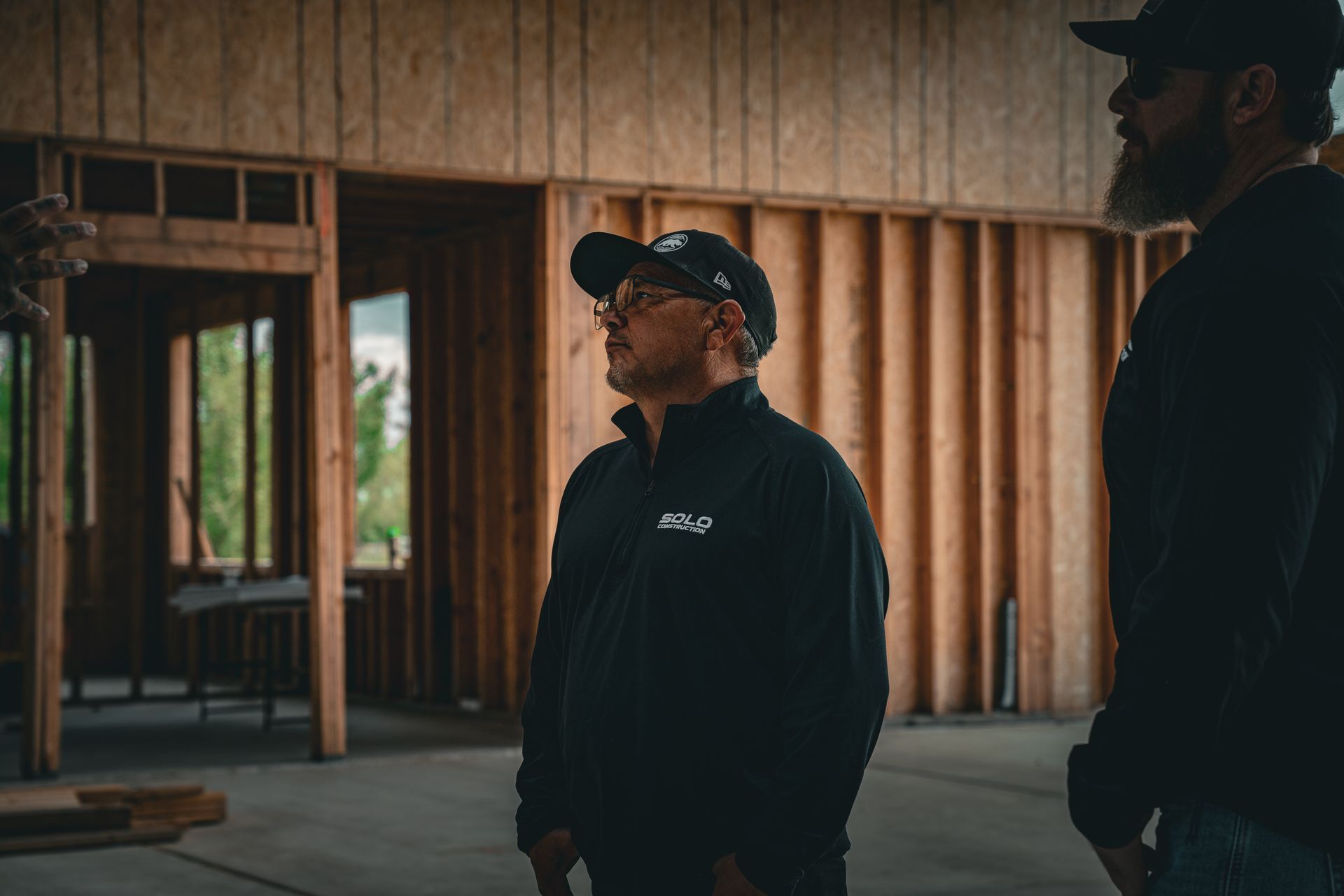 Two men in dark clothing standing in a wooden-framed building interior near an open doorway.