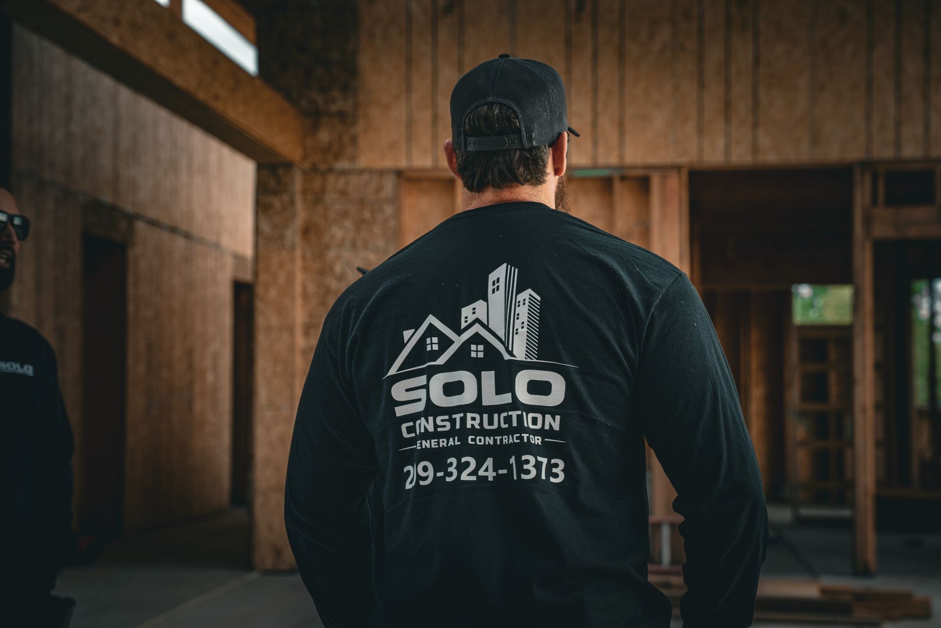 Man in a black hoodie with “SOLO Construction” logo, standing in a wooden-framed building interior.