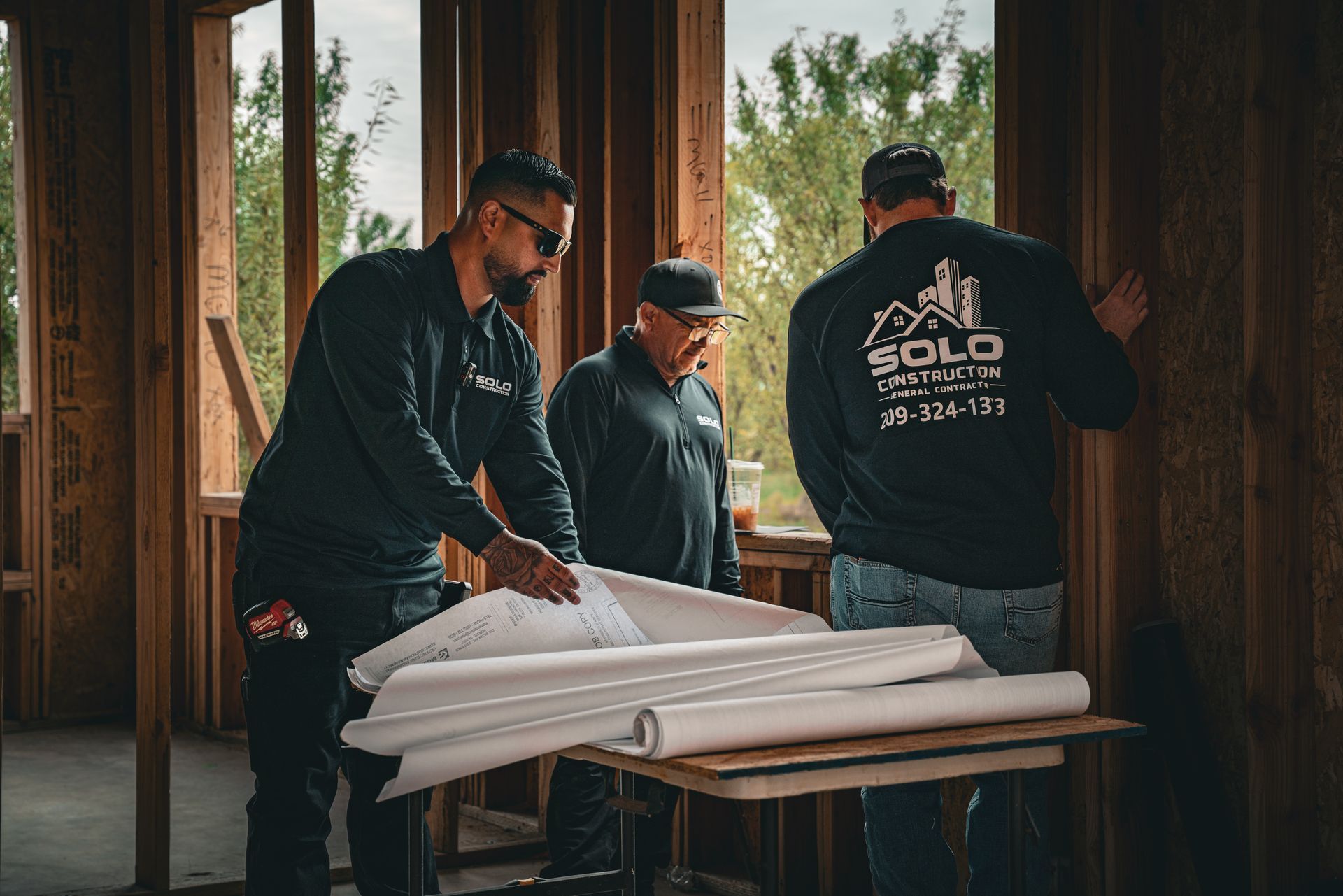 Three workers in dark clothing handling white insulation panels inside a wooden frame house.