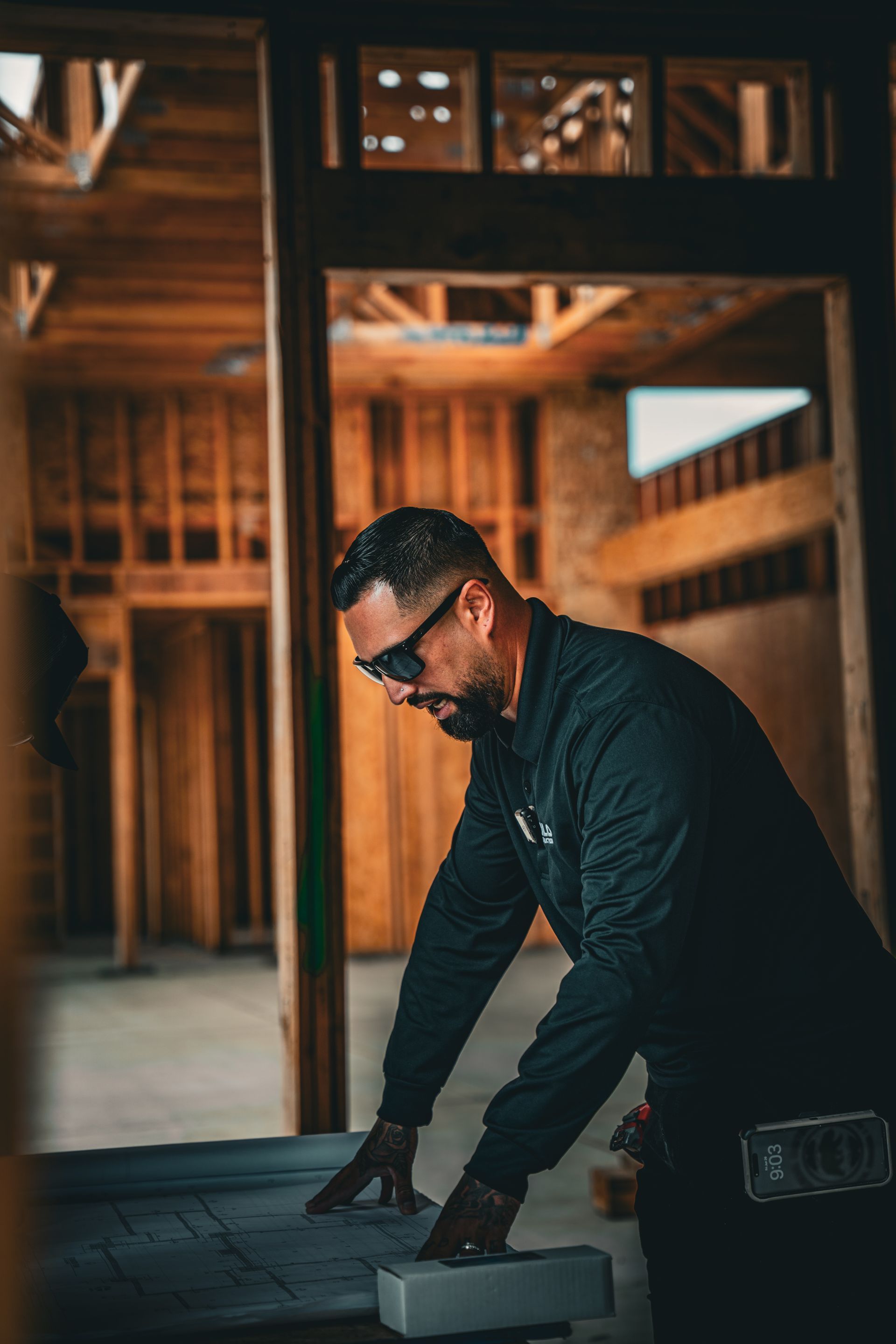 Man in black workwear measuring wood inside an unfinished wooden building
