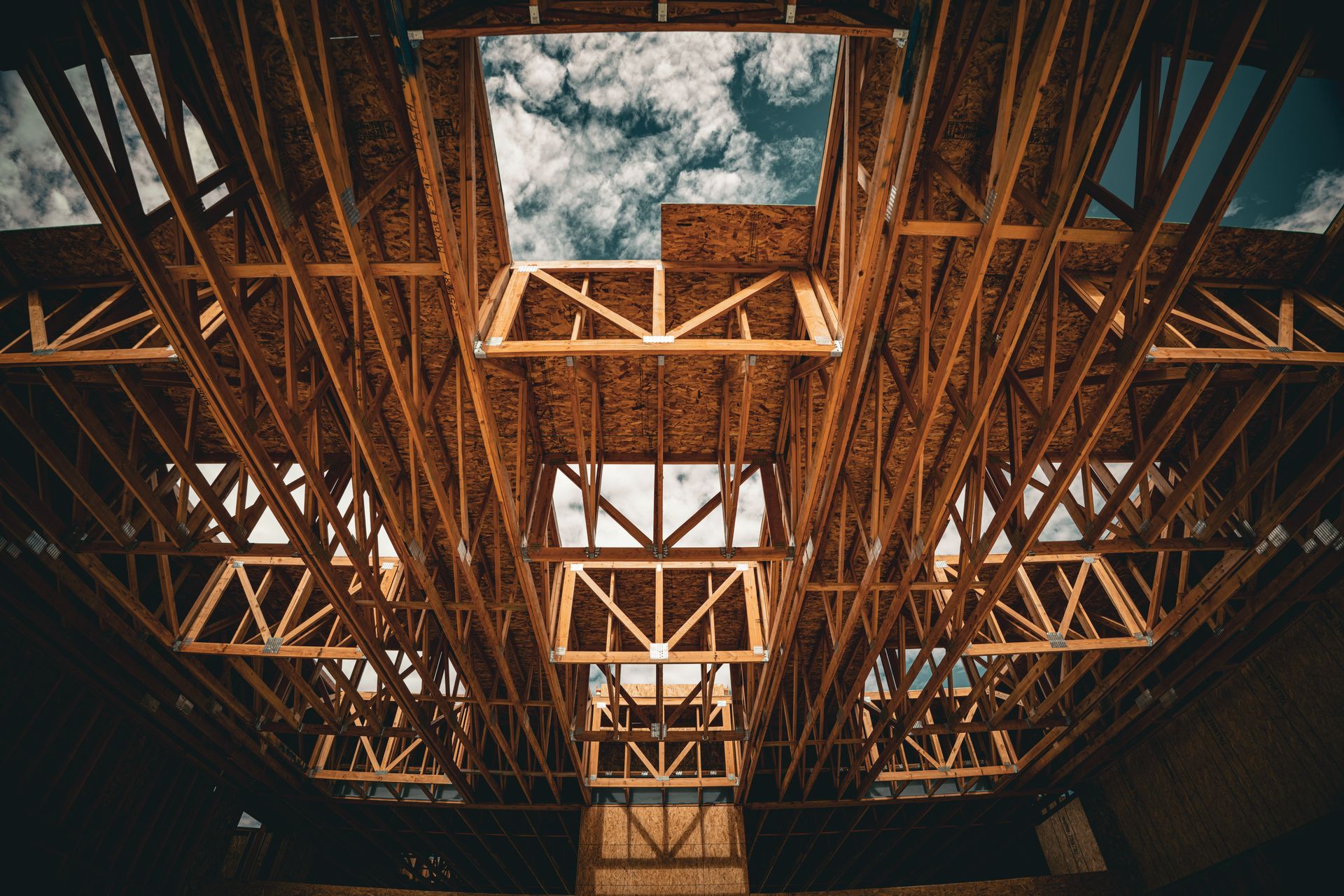 Interior view of a wooden framework ceiling with skylights and a cloudy sky above
