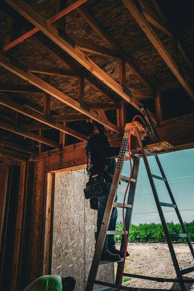 Worker on a ladder installing ceiling beams in a partially built structure outdoors