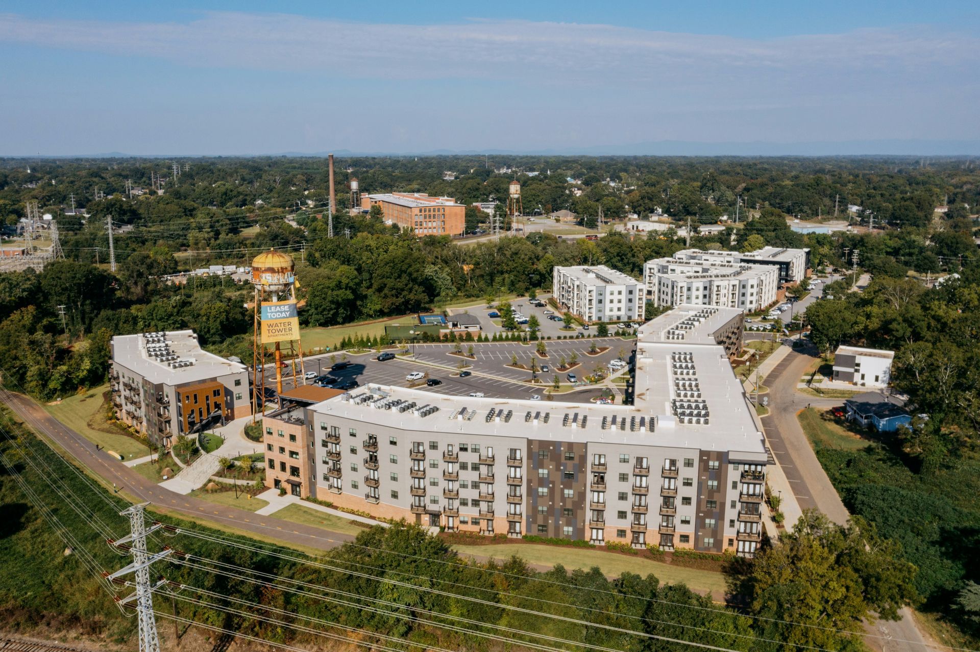 Aerial view of a large apartment complex with white buildings, a parking lot, and surrounding greenery.
