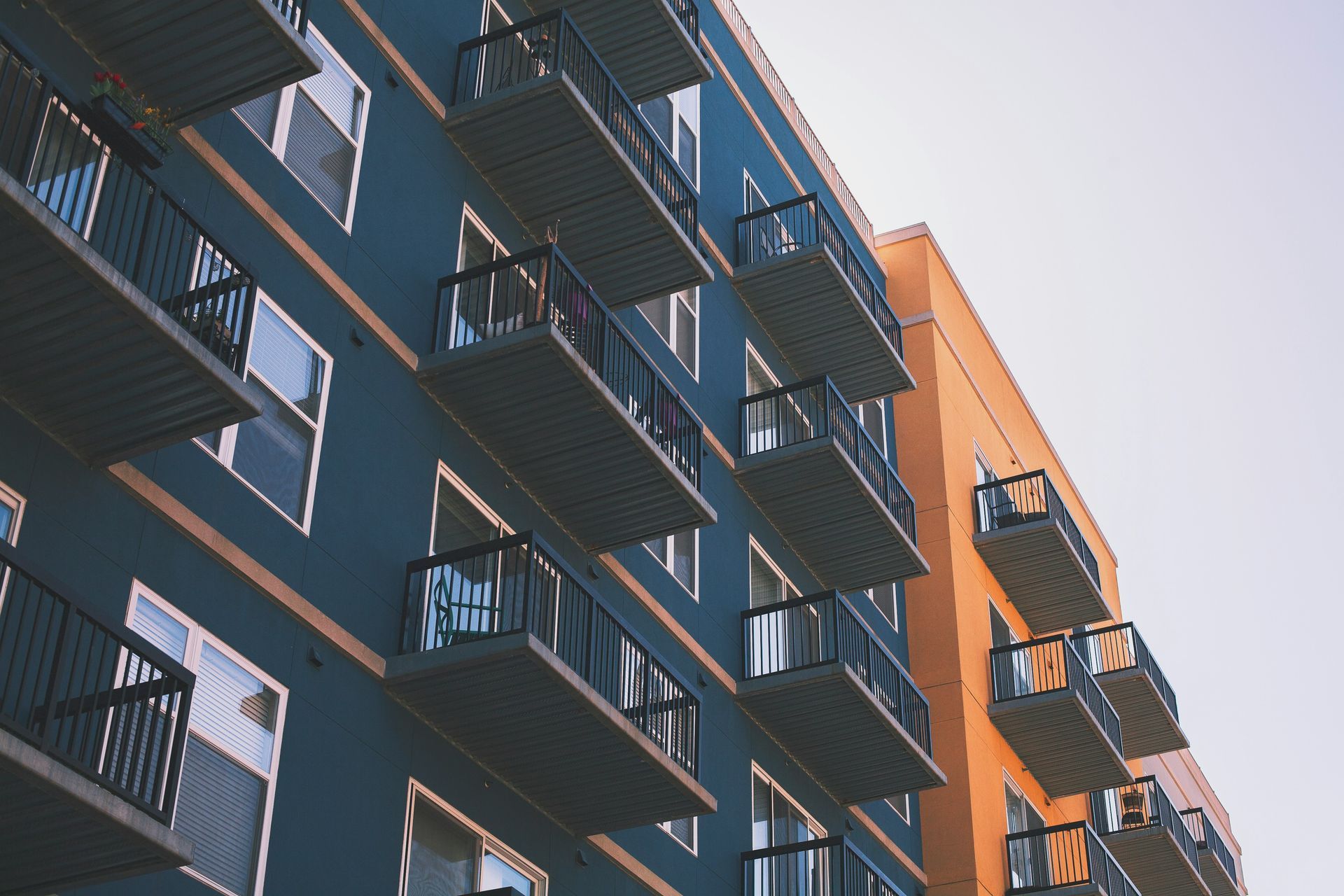 Apartment building balconies viewed from below against a blue sky.