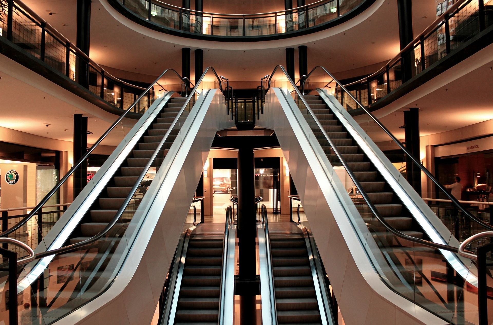 Symmetrical escalators in a brightly lit shopping mall atrium, viewed from below