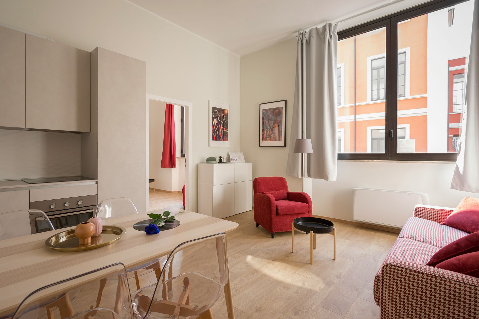Bright modern living room with red chairs, dining table, large window, and light curtains