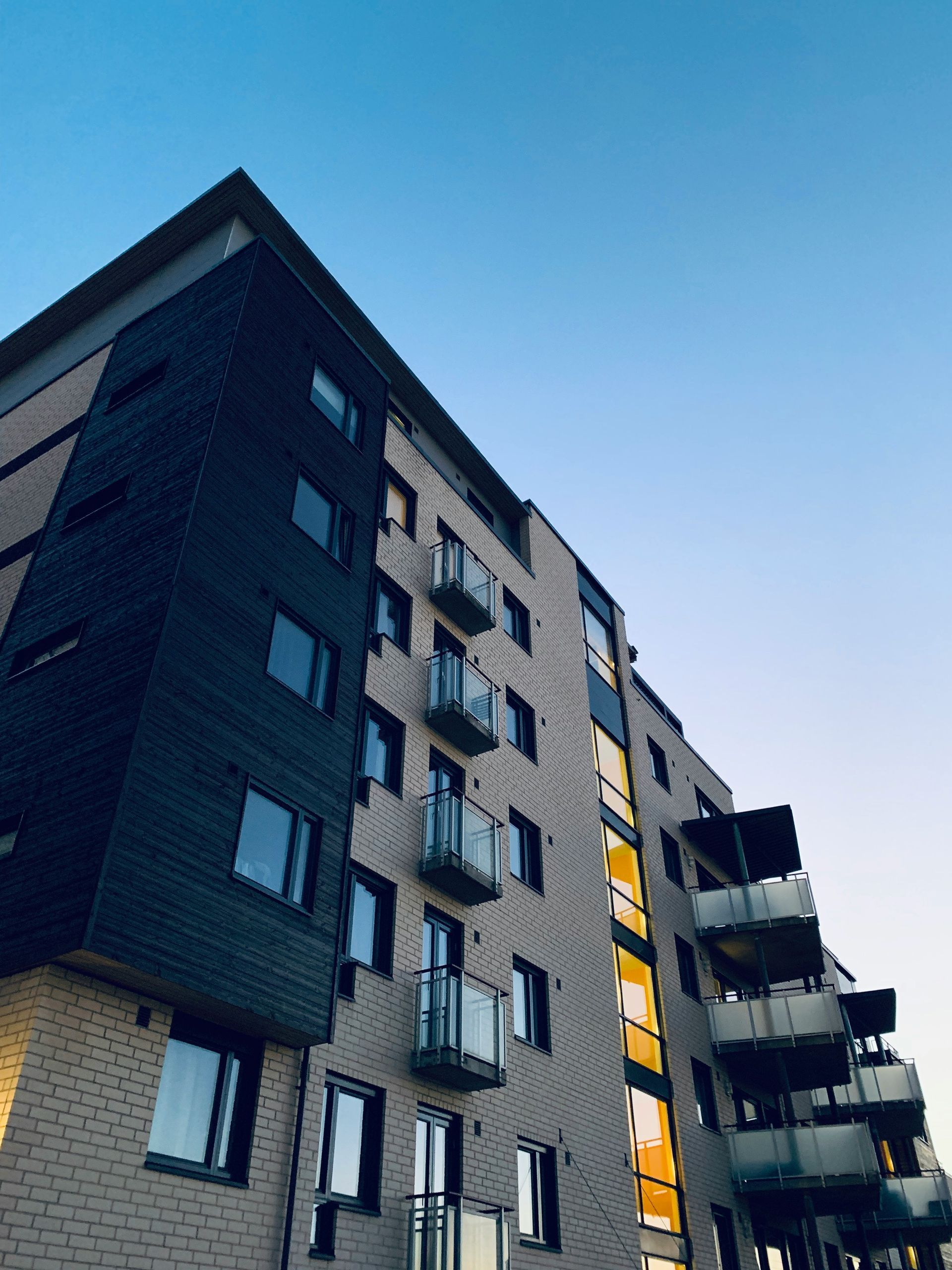 Low-angle view of a modern apartment building with dark and light facades and balconies against a blue sky