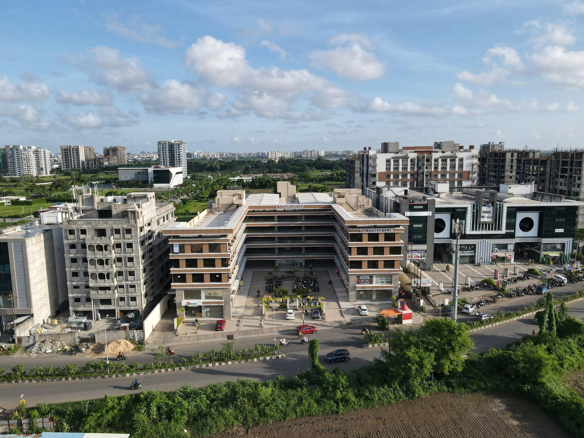 Cityscape with mid-rise buildings, a central unfinished structure, and a road under a partly cloudy sky.