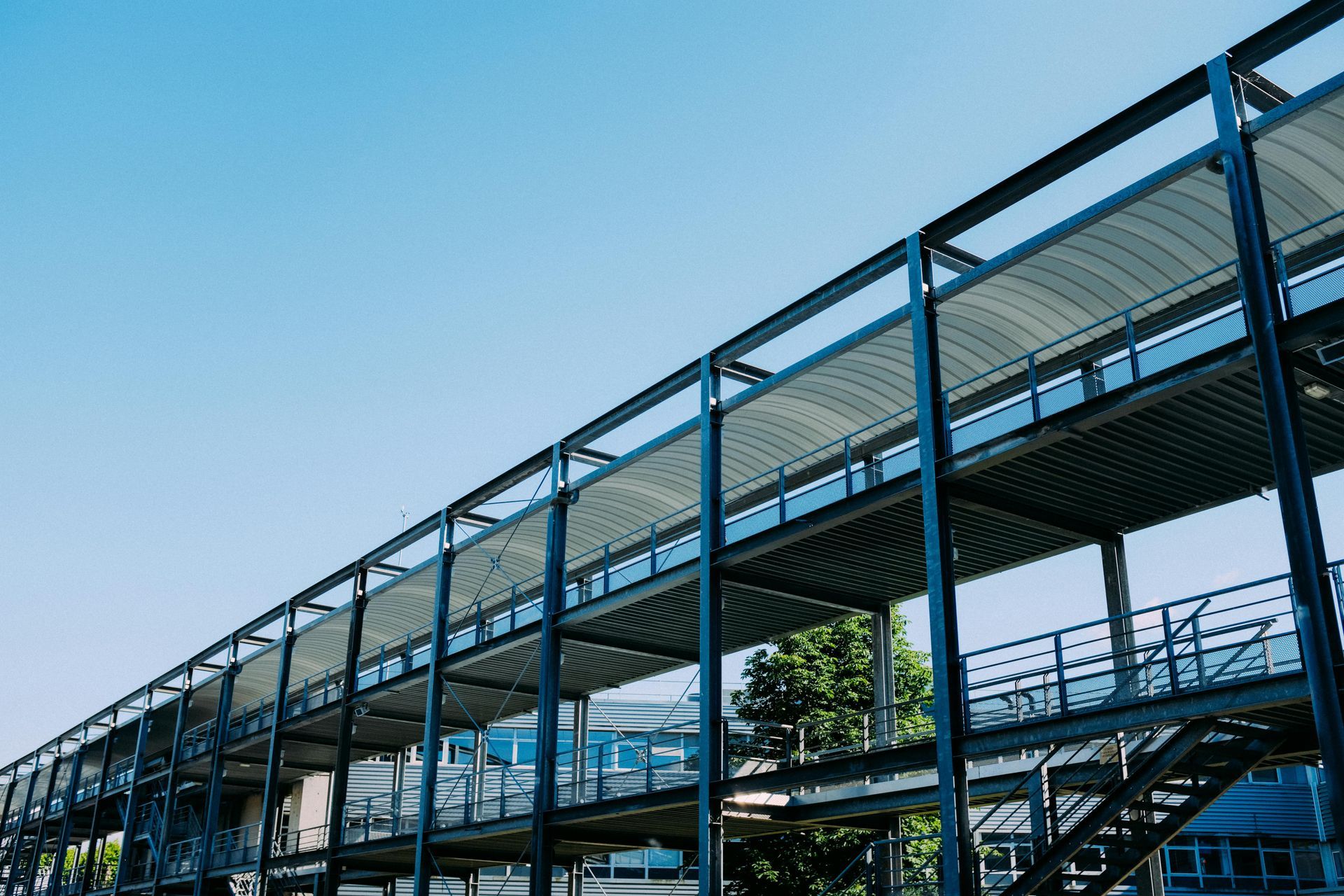 Empty metal pedestrian bridge walkway with blue railings under a clear sky