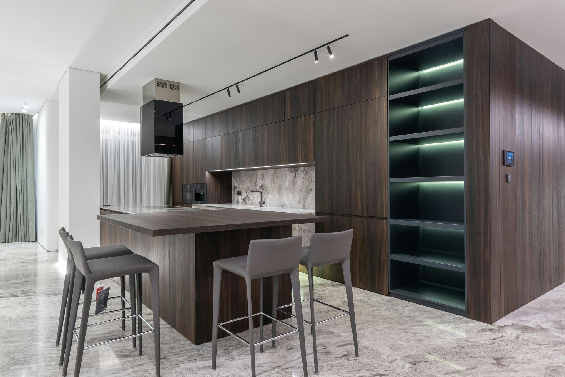 Modern kitchen with dark wood cabinetry, marble island, bar stools, and illuminated glass shelving