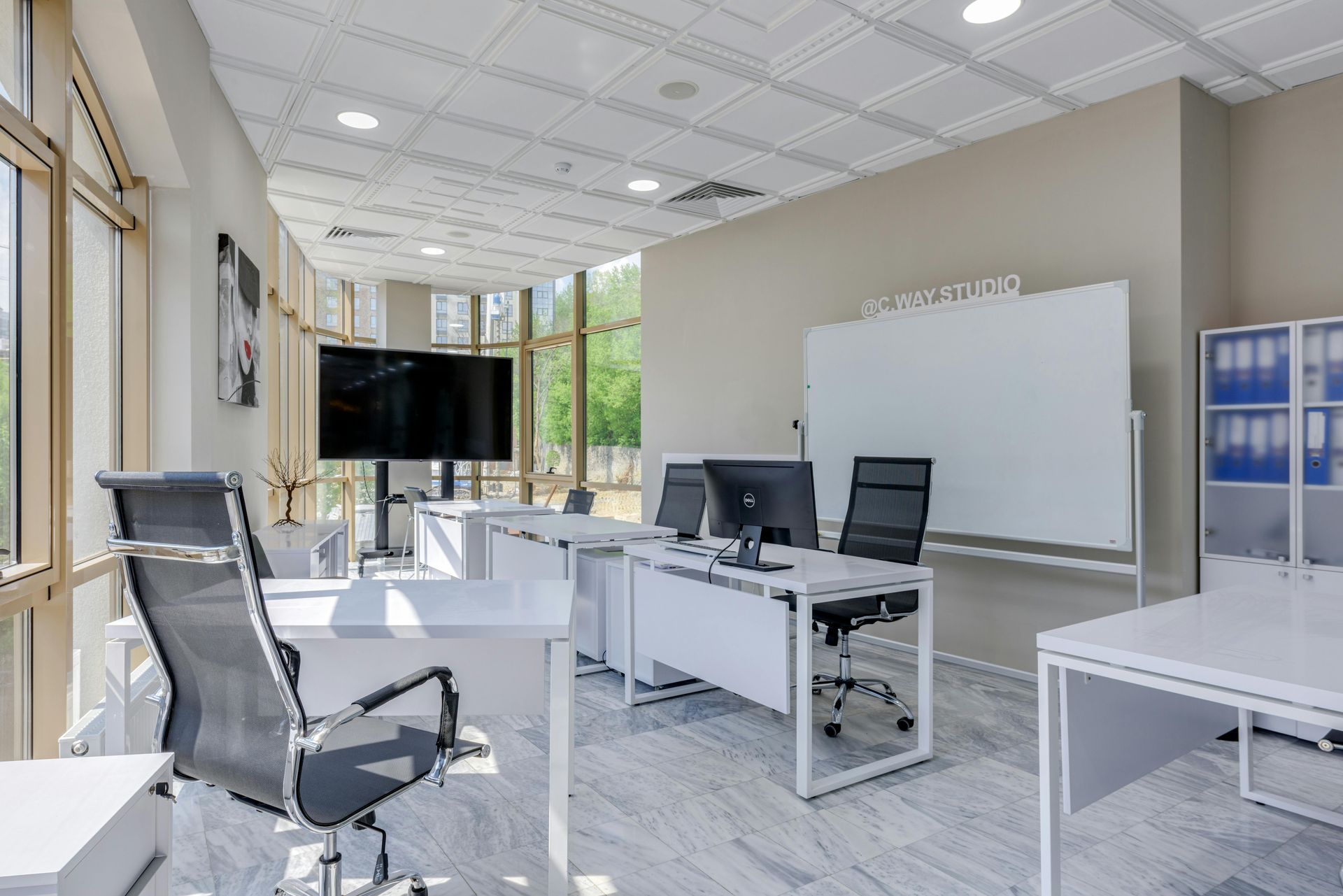 Modern office with desks, black chairs, whiteboard, computer, and bright windowed interior