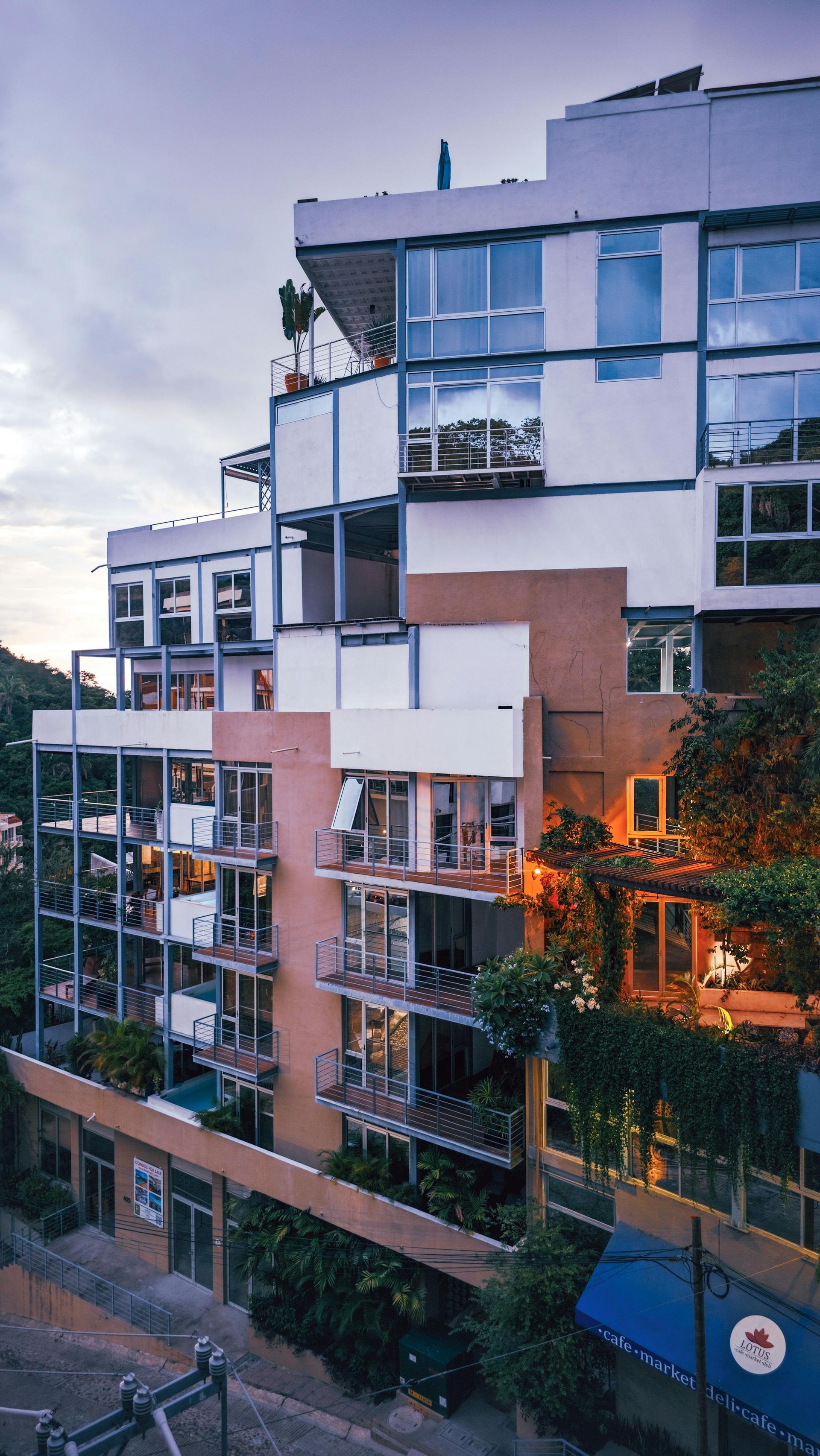 Modern apartment buildings at dusk with balconies, trees, and soft orange reflections in the windows
