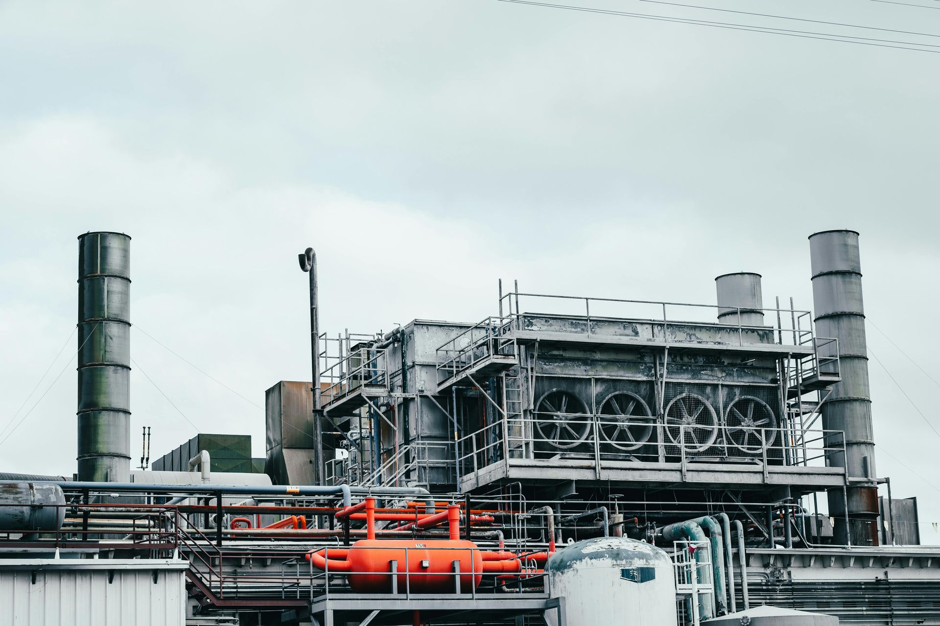 Industrial factory with tall smokestacks, pipes, and cooling fans under a gray sky