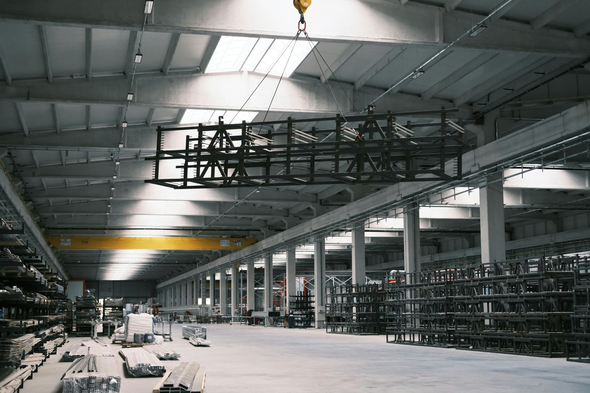 Large industrial warehouse interior with rows of shelving, a crane overhead, and scattered equipment on the floor