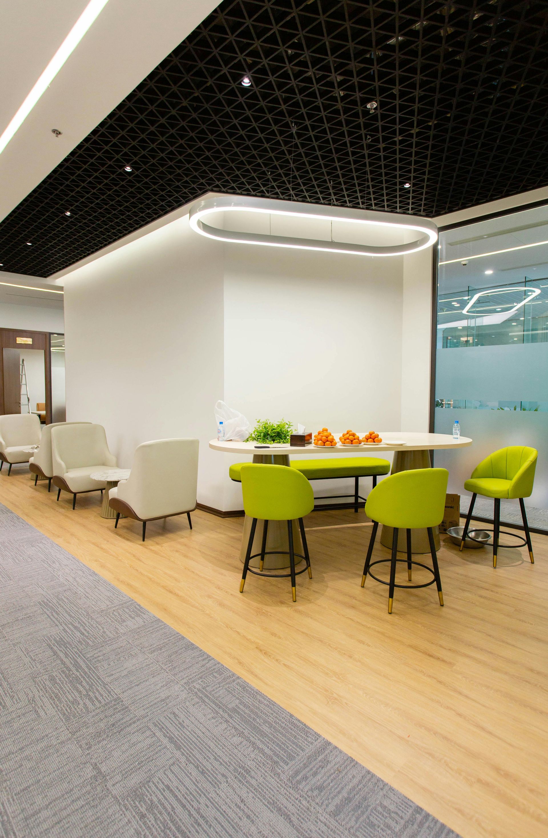 Modern office lounge with lime-green chairs, round table, and white seating area under a black ceiling