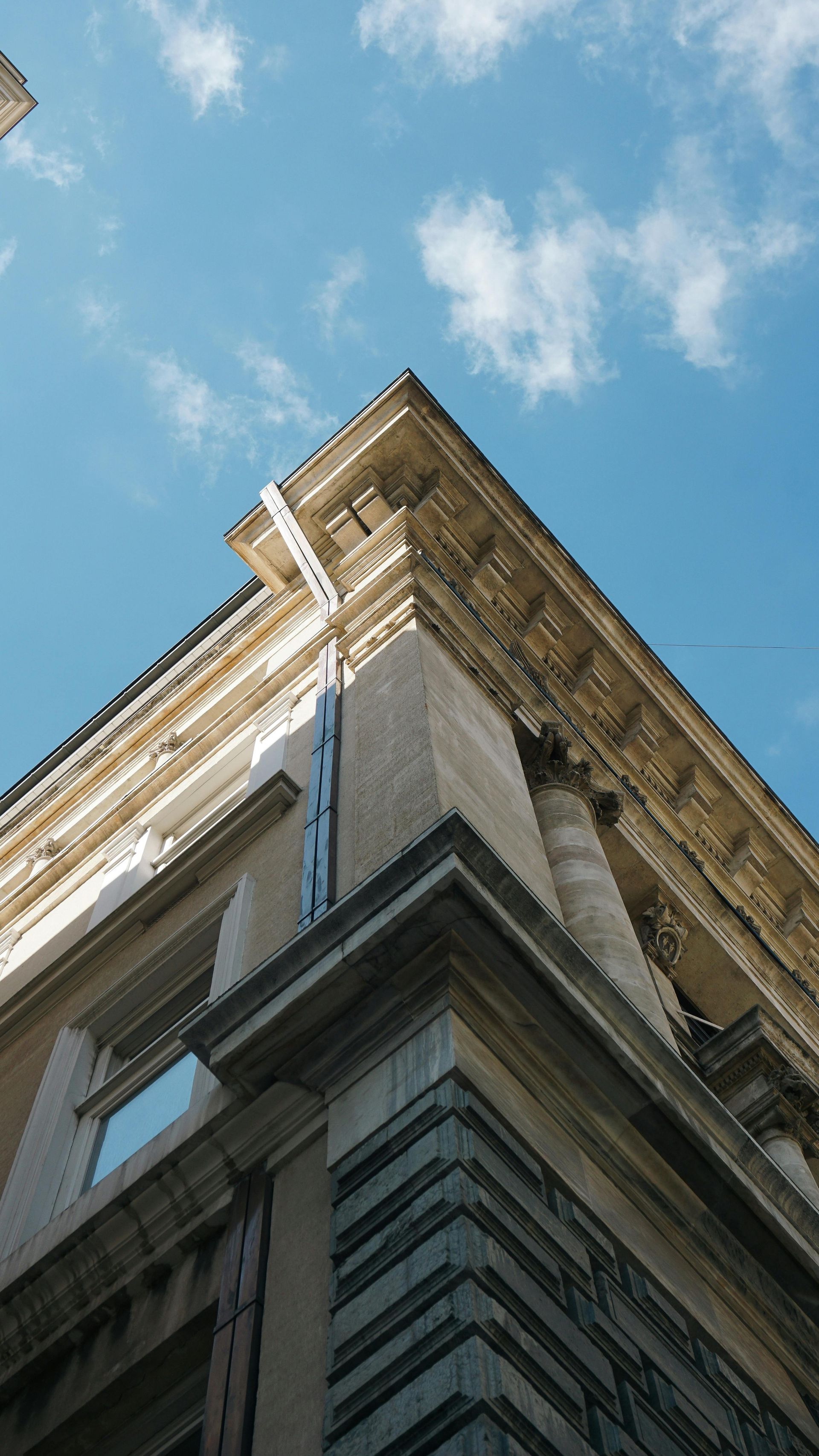 Corner of an old stone building against a blue sky with scattered clouds