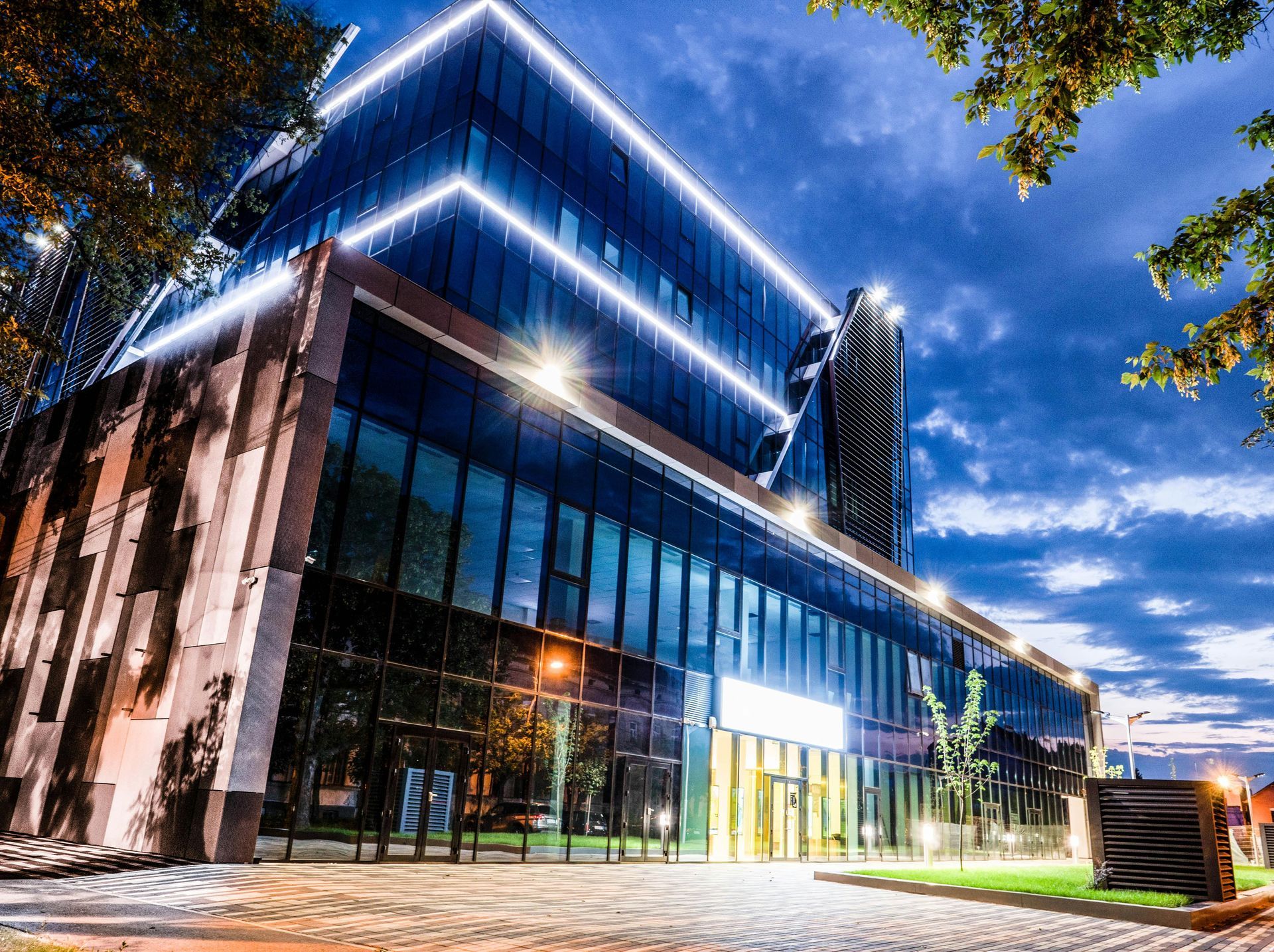 Modern glass office building at dusk with blue neon roof lights and a lit entrance