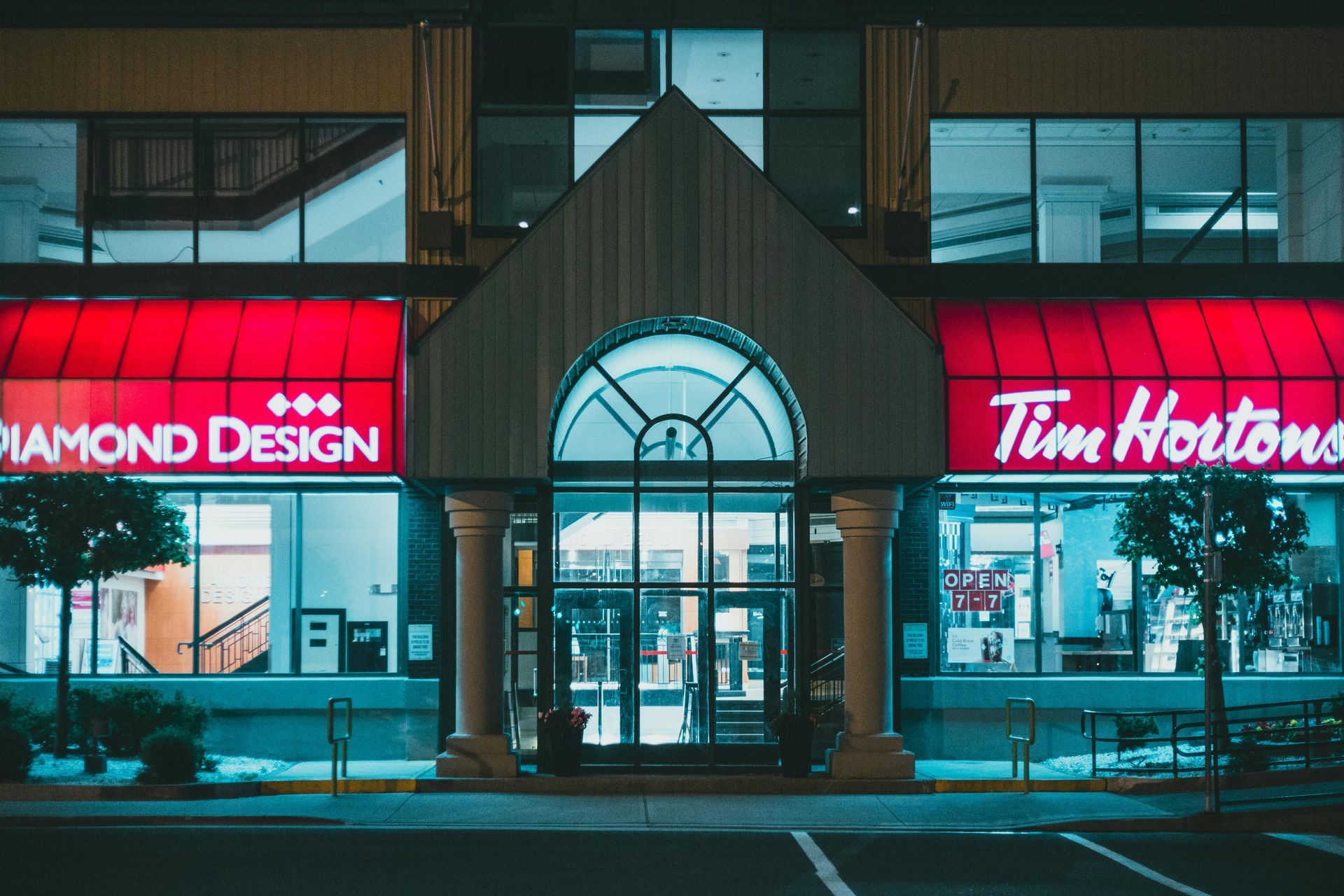 Night view of a Diamond Design storefront beside a Tim Hortons, with bright red neon signs and glass entrance.