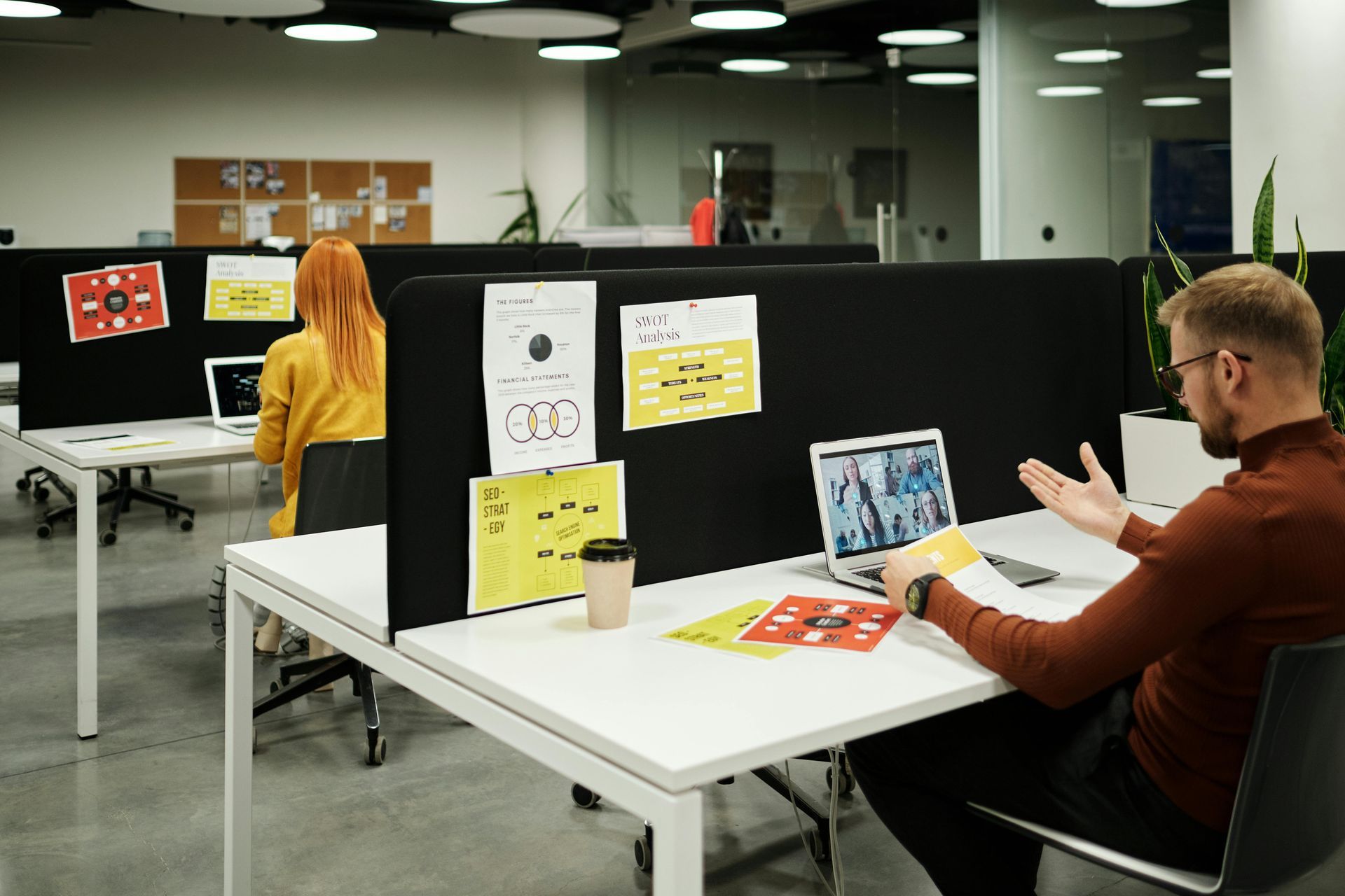 People in a modern office presenting posters at a long table with papers and a laptop