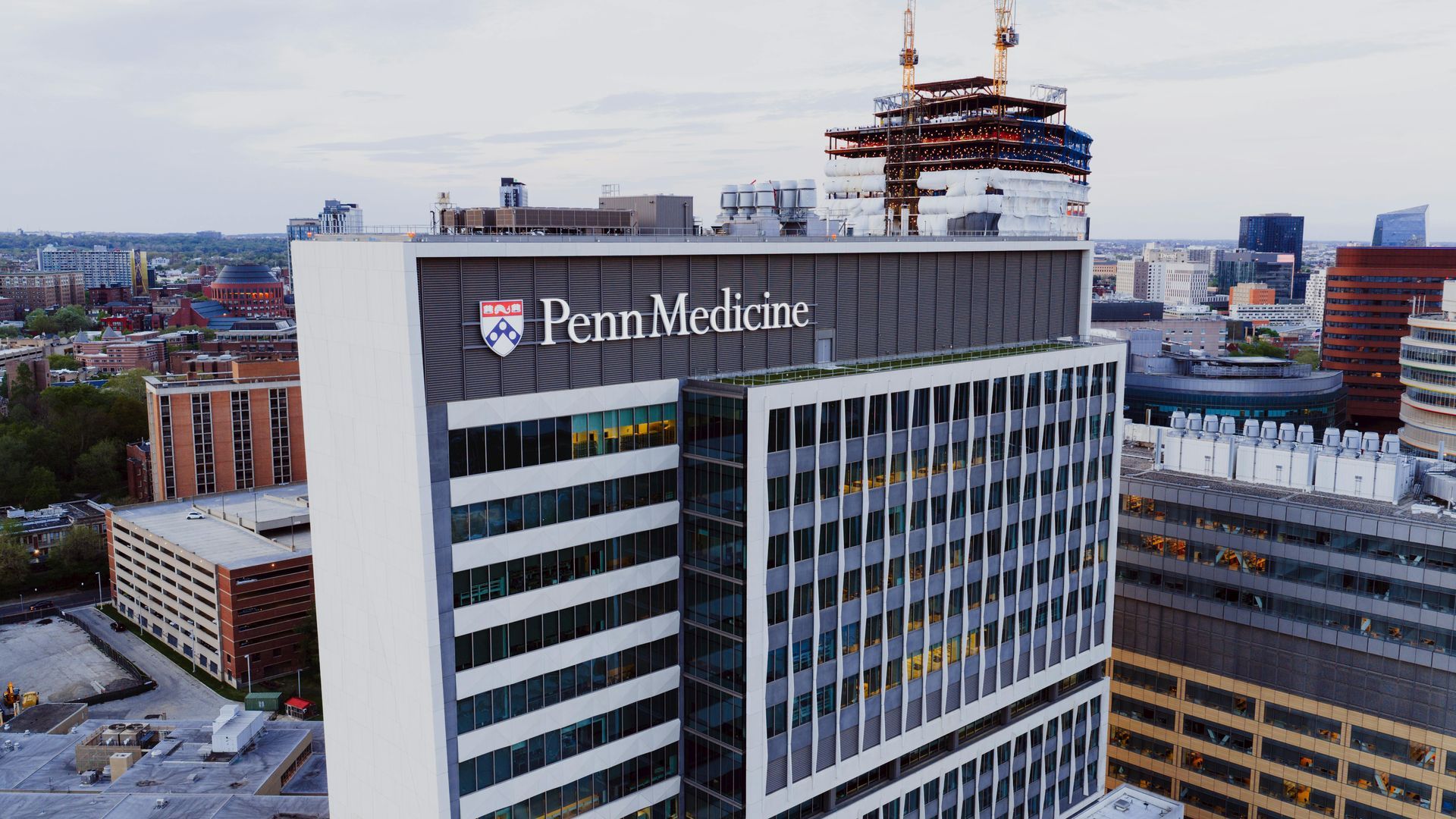 Penn Medicine hospital building with rooftop construction cranes in an urban skyline