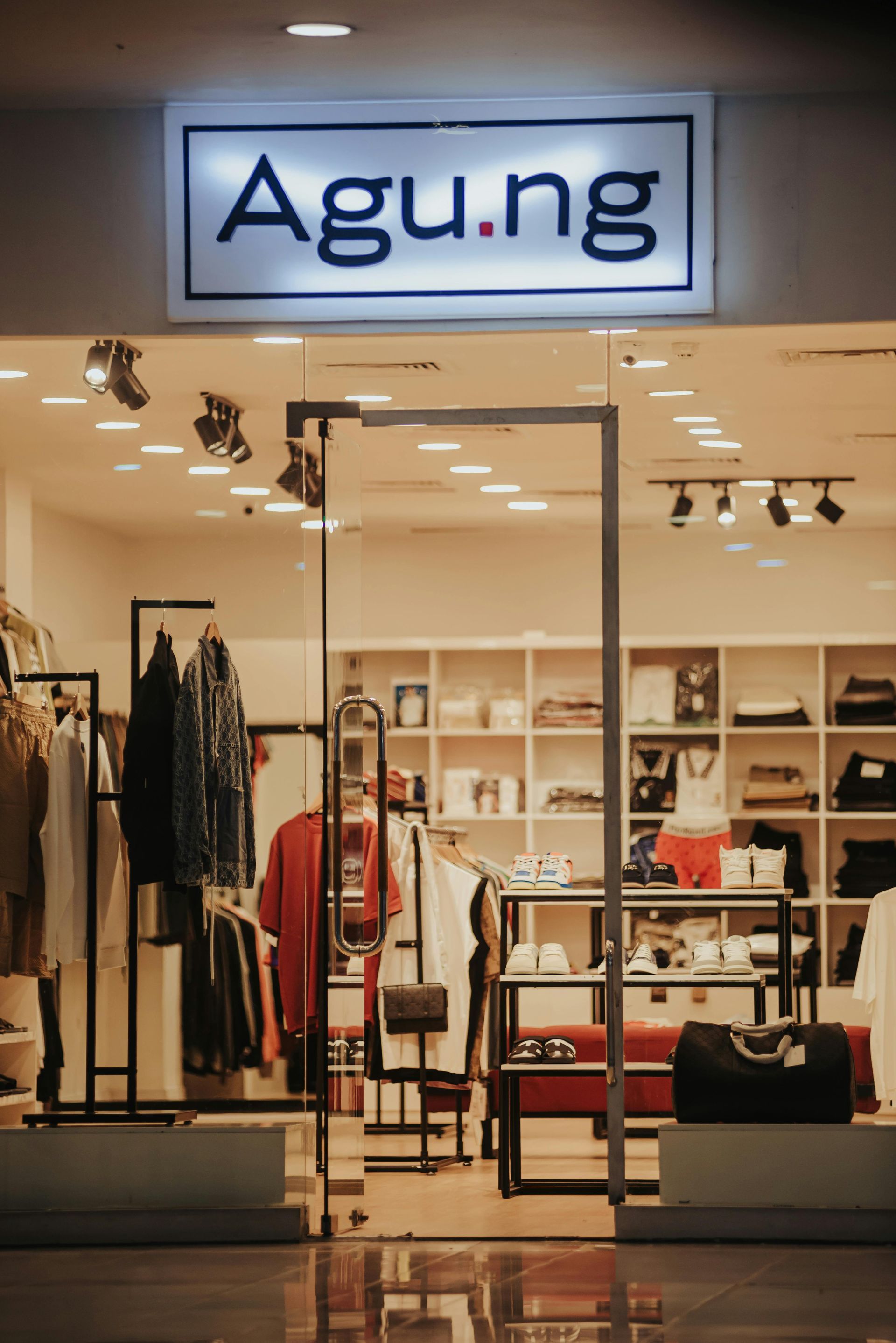 Agung clothing store storefront with illuminated sign and apparel displays behind glass