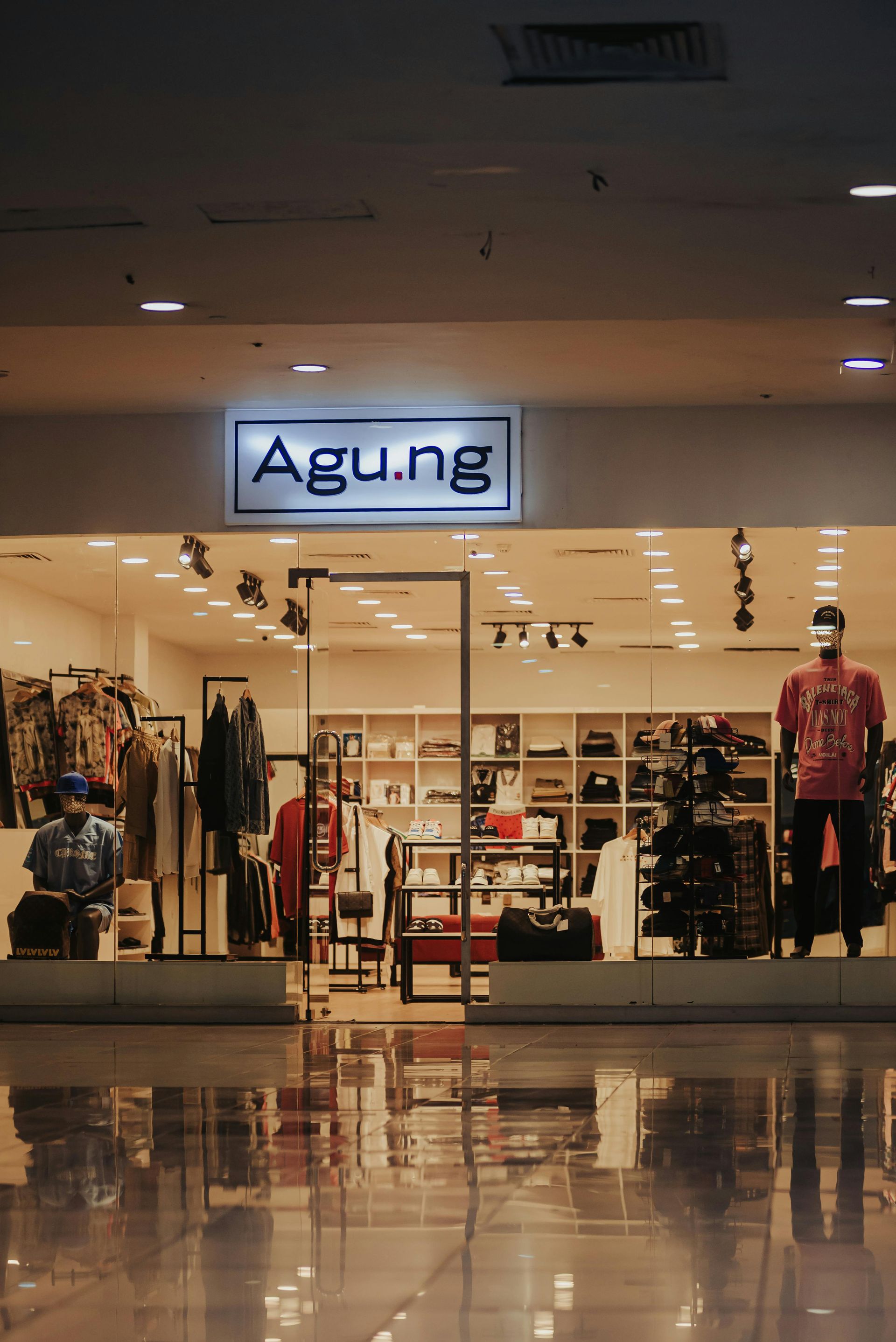 Clothing store storefront with illuminated Agu.ng sign and racks of apparel visible inside