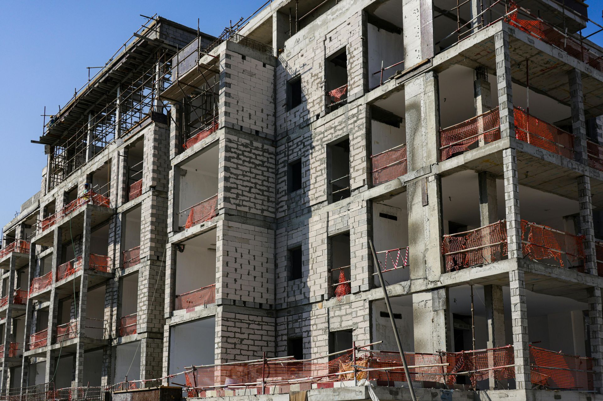 Partially built apartment complex with concrete floors, scaffolding, and orange safety netting