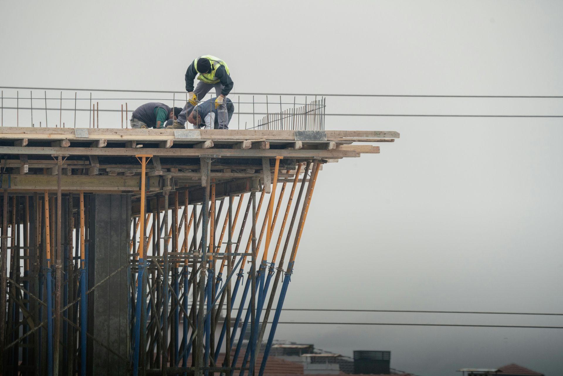Construction workers on a high-rise platform, installing rebar near the edge in a foggy setting