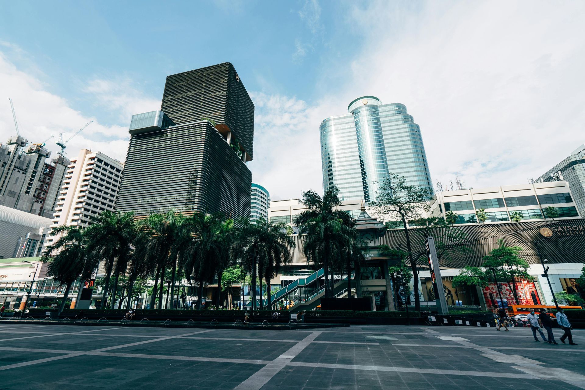 Modern city plaza with palm trees and tall office towers under a cloudy sky