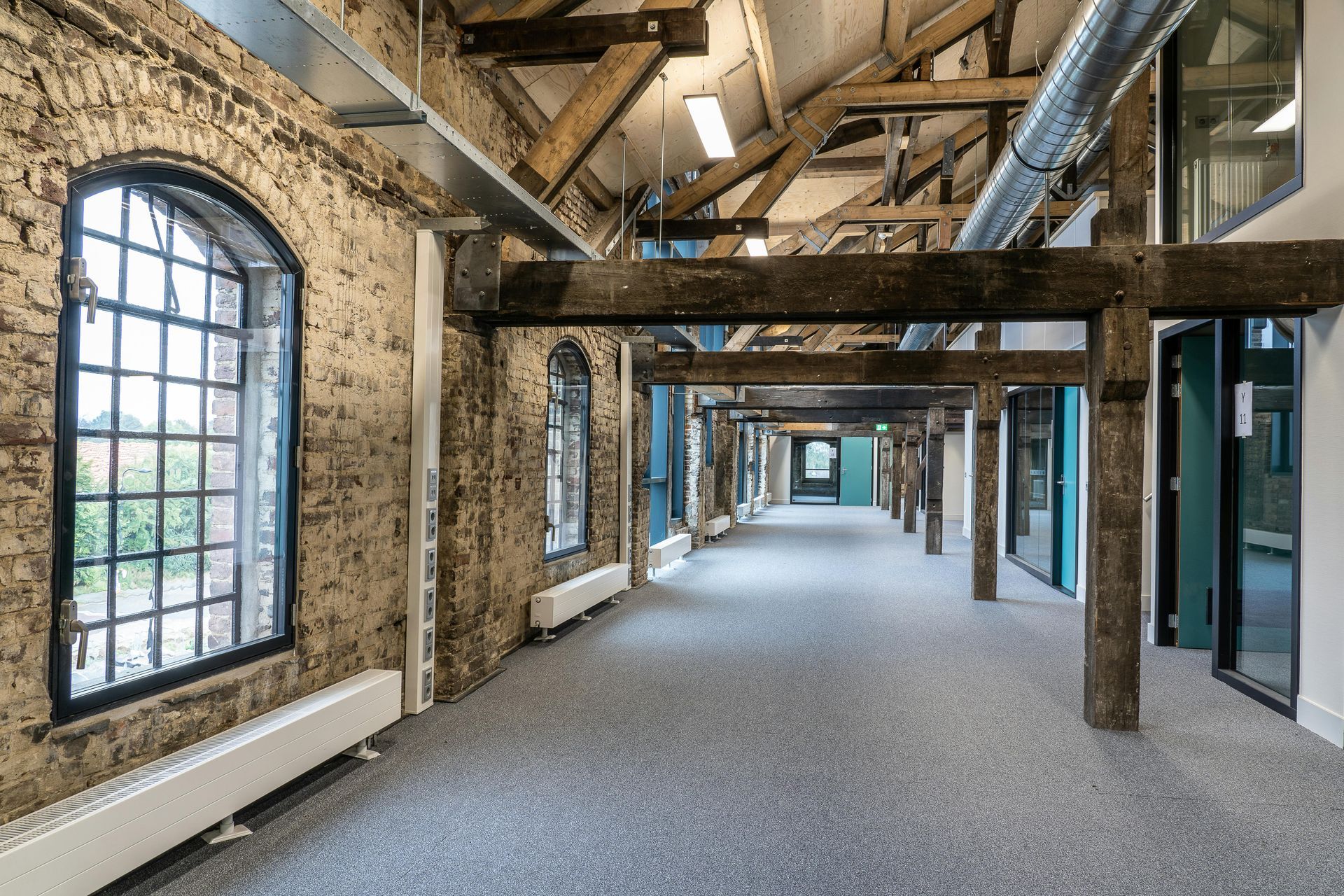 Empty industrial loft corridor with exposed beams, arched windows, and concrete floor